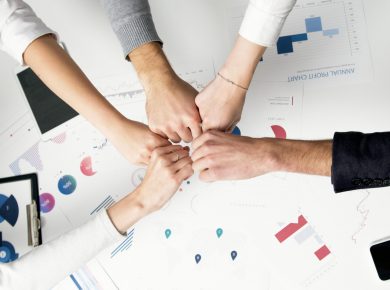Free Colleagues celebrate success with a fist bump over financial charts depicting teamwork and unity. Stock Photo